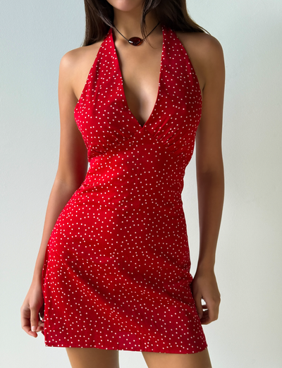 A woman stands against a plain light-colored background wearing the Tiger Mist CL - DYLAN HALTER MINI DRESS, a sleeveless red halter-neck mini dress with white polka dots.