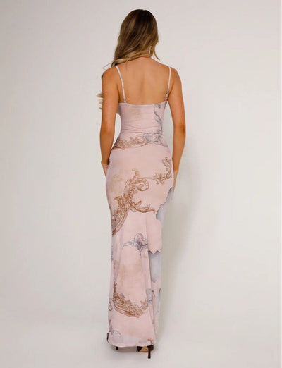 A woman with long, wavy hair models the JULIANNA DRESS - MULTI : COLLAGE : CRANES by TIGERMIST, a sleeveless maxi dress, standing against a plain light background and facing away from the camera.