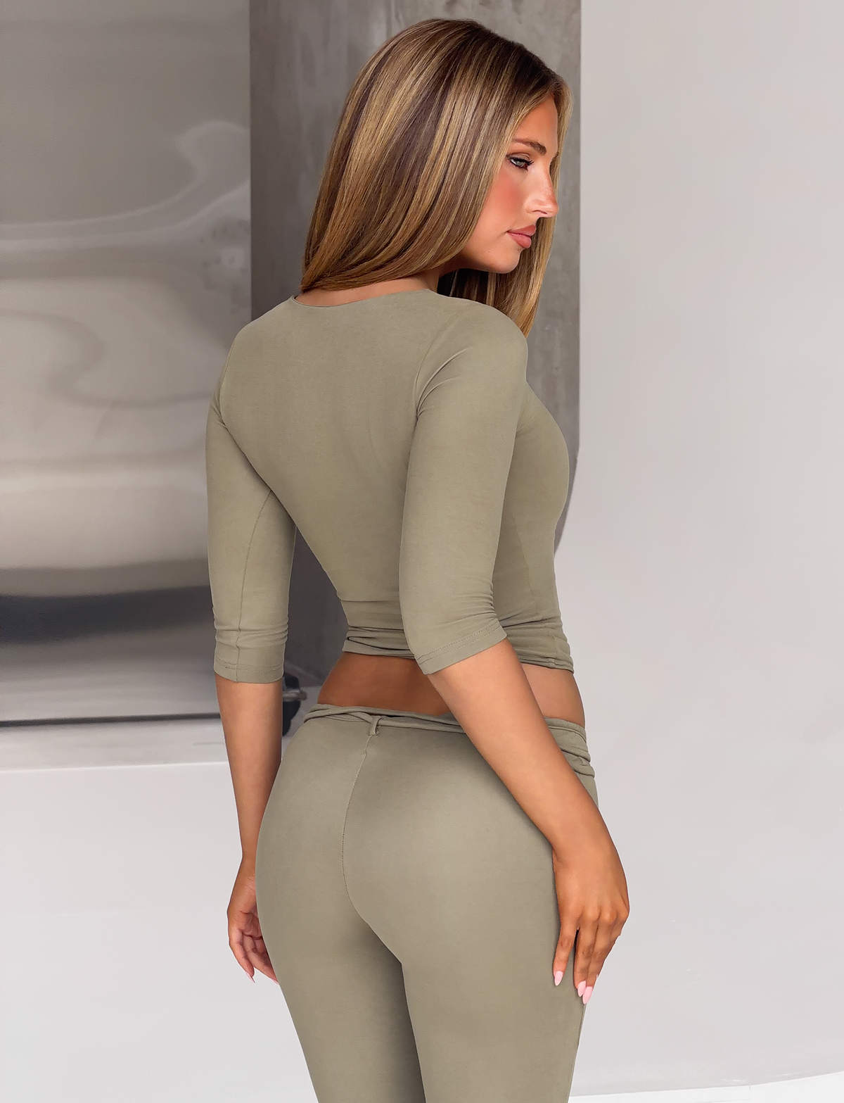 A woman wearing a KHORA TOP - OLIVE featuring a beaded keyhole cutout, paired with matching olive green leggings.