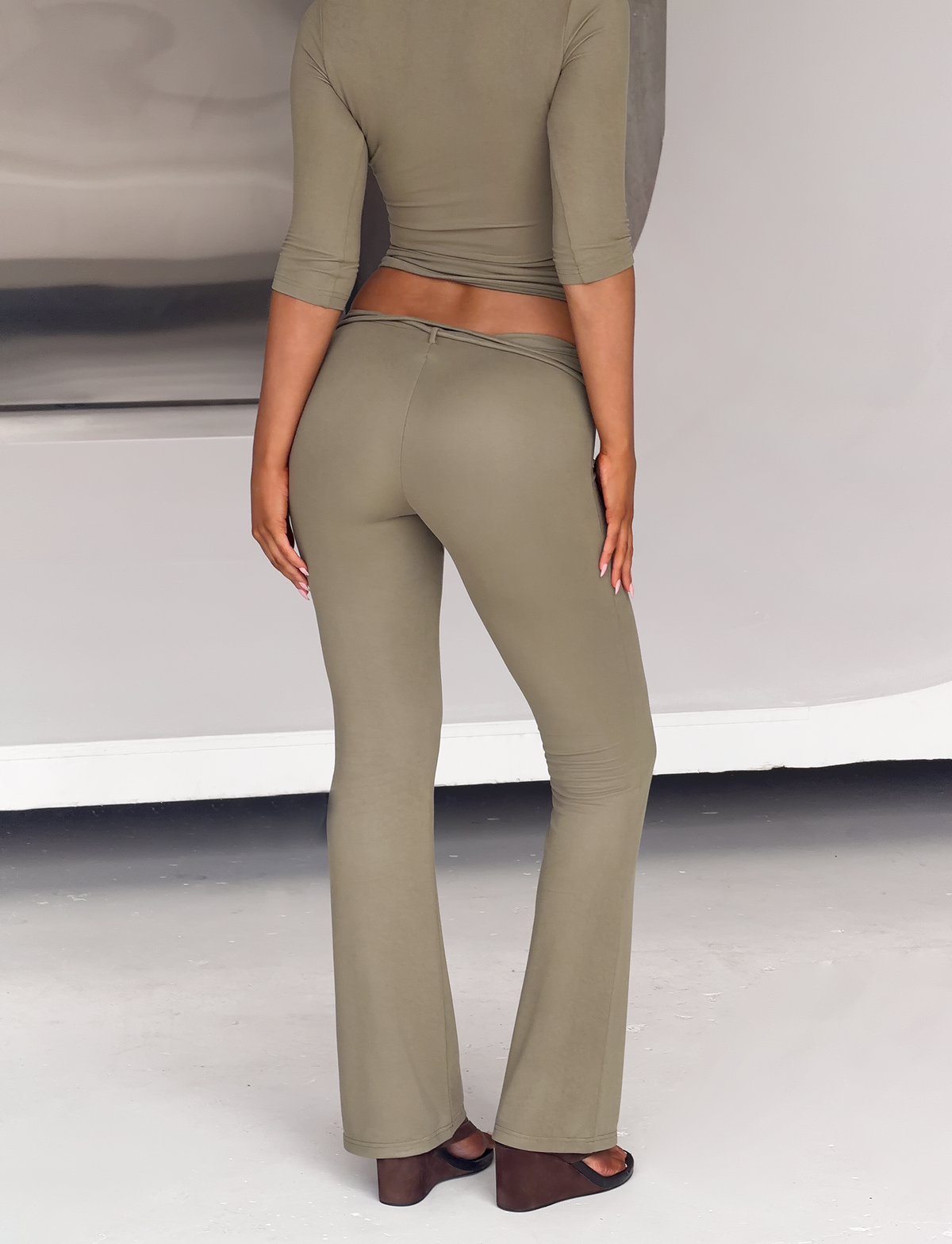 Back view of a person wearing the olive green KHORA PANT, featuring a matching three-quarter sleeve top with a beaded self belt and mid-rise, flared pants.