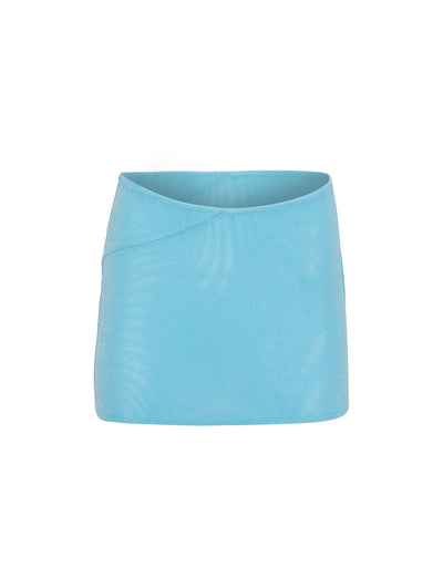 The COBI SKIRT - SHIMMER from TIGERMIST is shown in a light blue, high-waisted mini skirt design. It features a subtle shimmer finish and boasts a clean, minimalistic appearance with a slight asymmetrical seam on the left side, adding an elegant touch of detail to the smooth fabric.