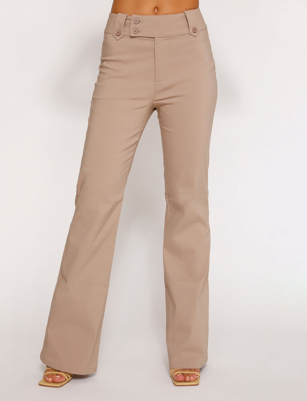 A person is modeling the Kittie High Rise Pant in beige from Tigermist, featuring a double-button closure. The pants have a clean, tailored fit and are styled with open-toe heels against a plain white background. The model’s upper body is not visible.