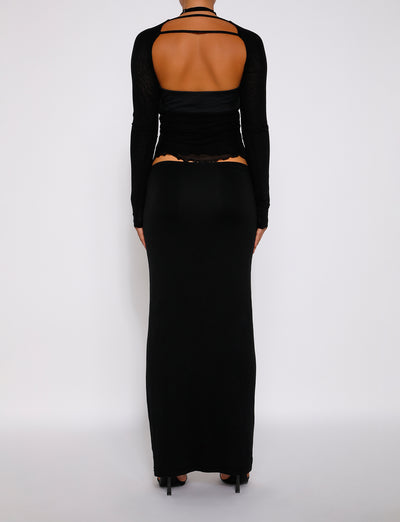 Back view of a person wearing the long-sleeve top with an open back paired with TigerMist's ADDISON SKIRT in black. They are standing against a plain white background, showcasing the clothing details and design. The person is wearing black high-heeled shoes.